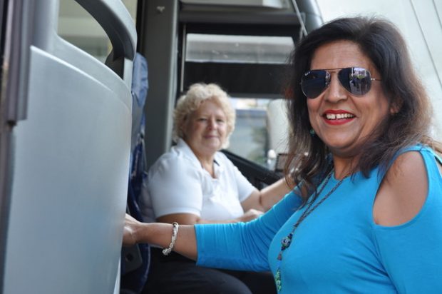 Lady smiles as she gets on Comfort Tour bus, driver smiles in background.