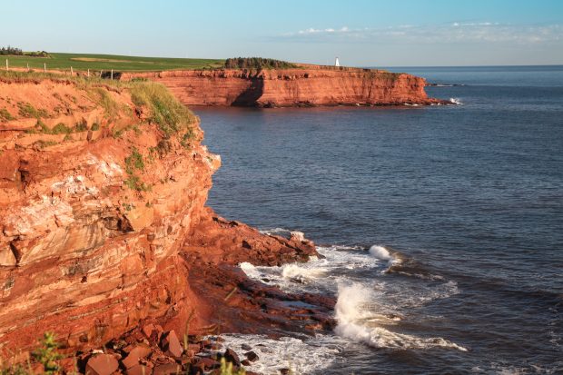 The rocky shore of Prince Edward Island at daybreak illuminating the cliffs and rocks bright red as seen on the East Coast bus tour.